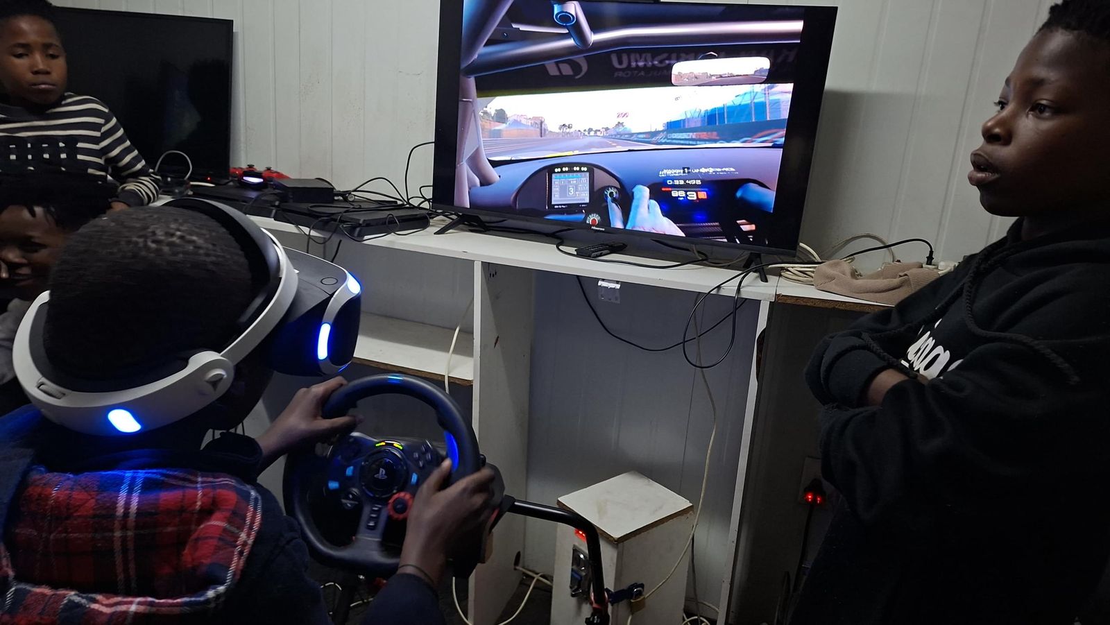 A player in a VR headset races while friends watch the screen